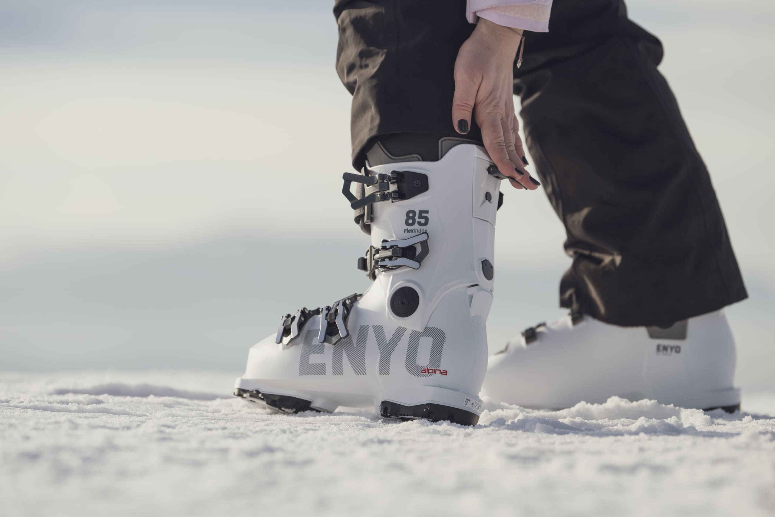 Female skier on snow putting on ski boot with expandable cuff for a comfortable, secure fit.