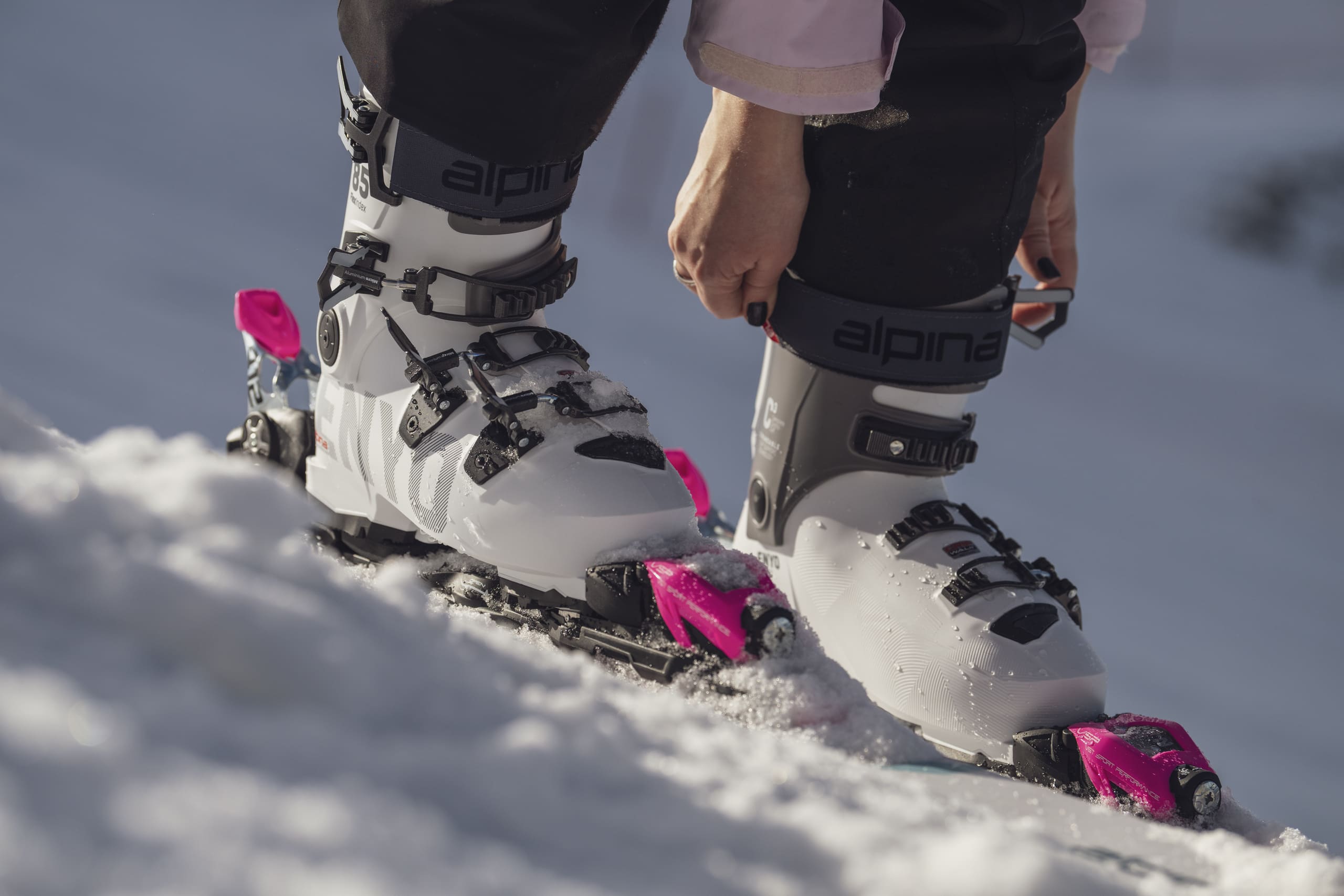 On-snow shot of a female skier in white Enyo ski boots, with a textured surface that echoes the feel of a pristine ski run.