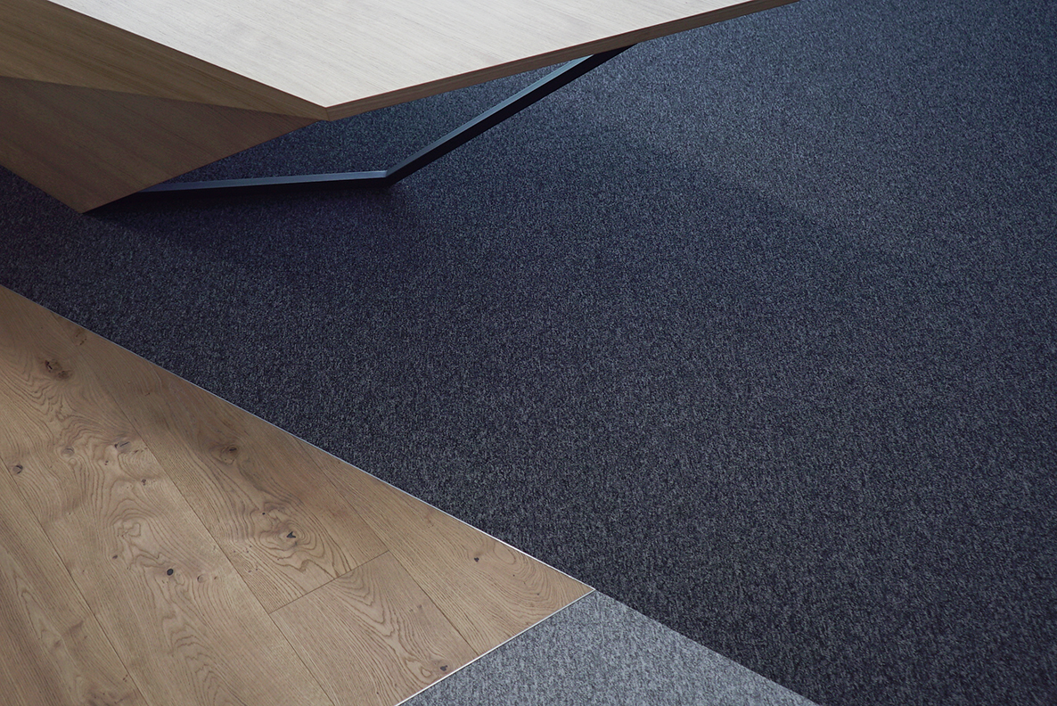 A photo of the Mebor company executive office space interior design, showing the custom flooring detail, diagonal cuts separting wood flooring with two tones of textile flooring.